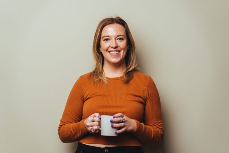 Lizzie Benton wearing an orange jumper, holding a mug of (probably) tea.
